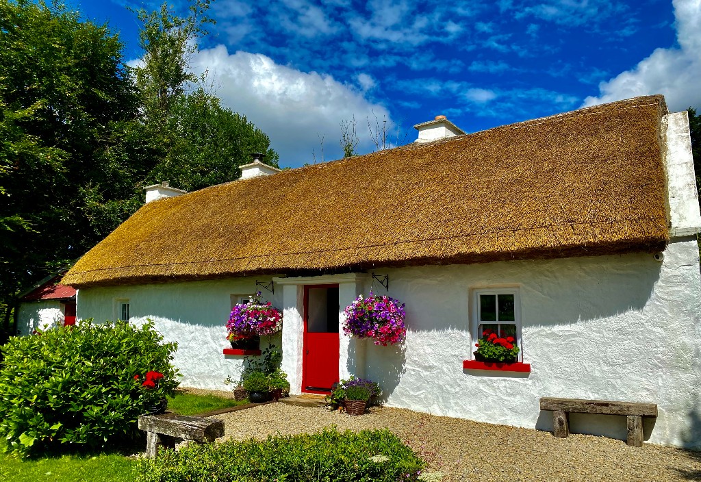 Traditional whitewashed thatched cottage with red trim and flower baskets in County Fermanagh.