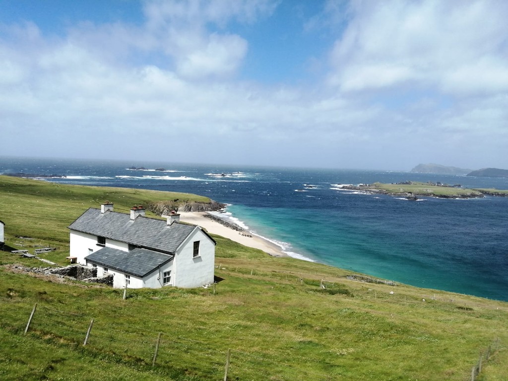 Remote white cottage overlooking a small beach and turquoise Atlantic waters on the Great Blasket Island, County Kerry.