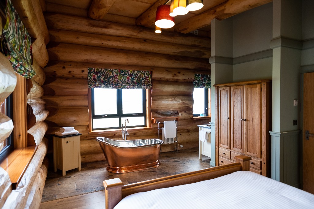 Rustic log cabin interior with a freestanding copper bath and woodland views in County Antrim.