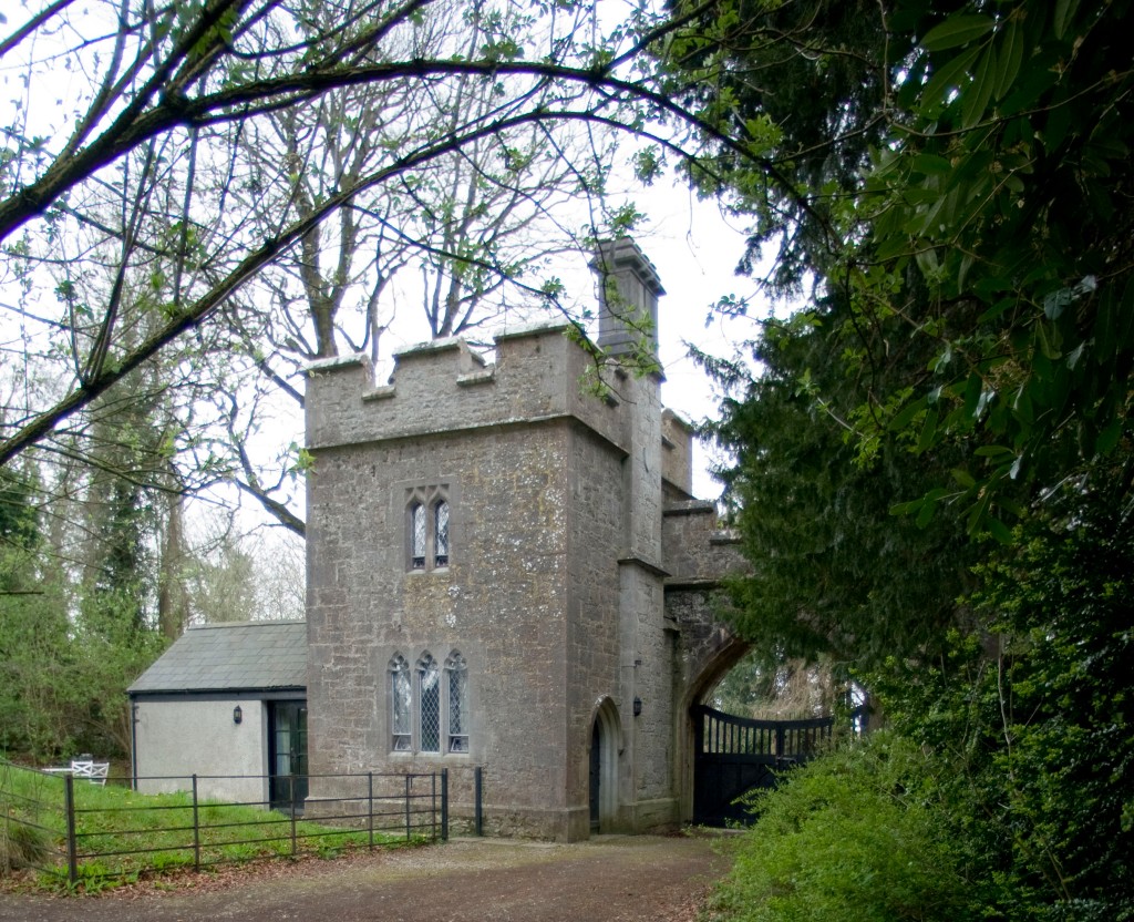 Gothic-style stone gatehouse with turret nestled among trees in County Cork.