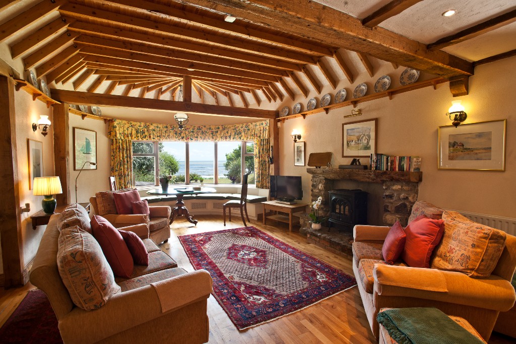Cosy living room with timber beams, stone fireplace and bay window looking out to the sea in County Meath.