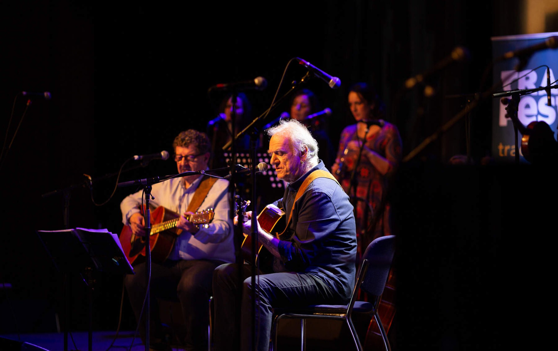 TradFest performers play string instruments and sing under dramatic lighting inside a Temple Bar venue in Dublin city.