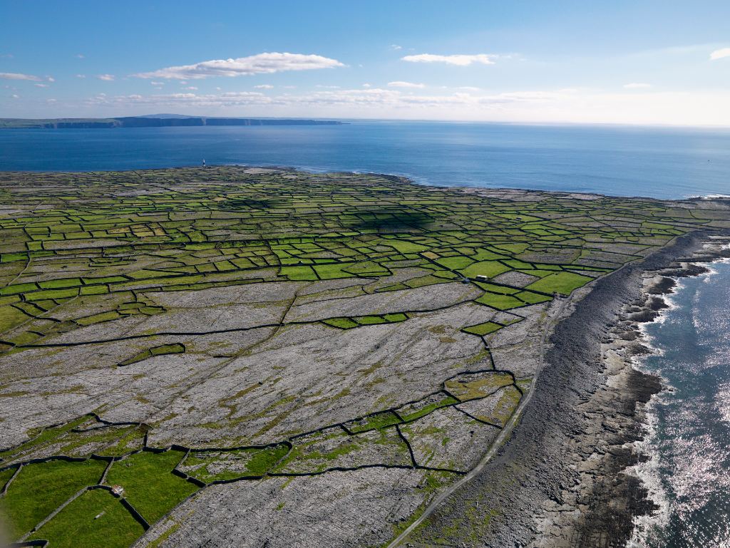 An aerial view of Inis Oírr shows stone-walled fields and Atlantic coastline under a clear summer sky.