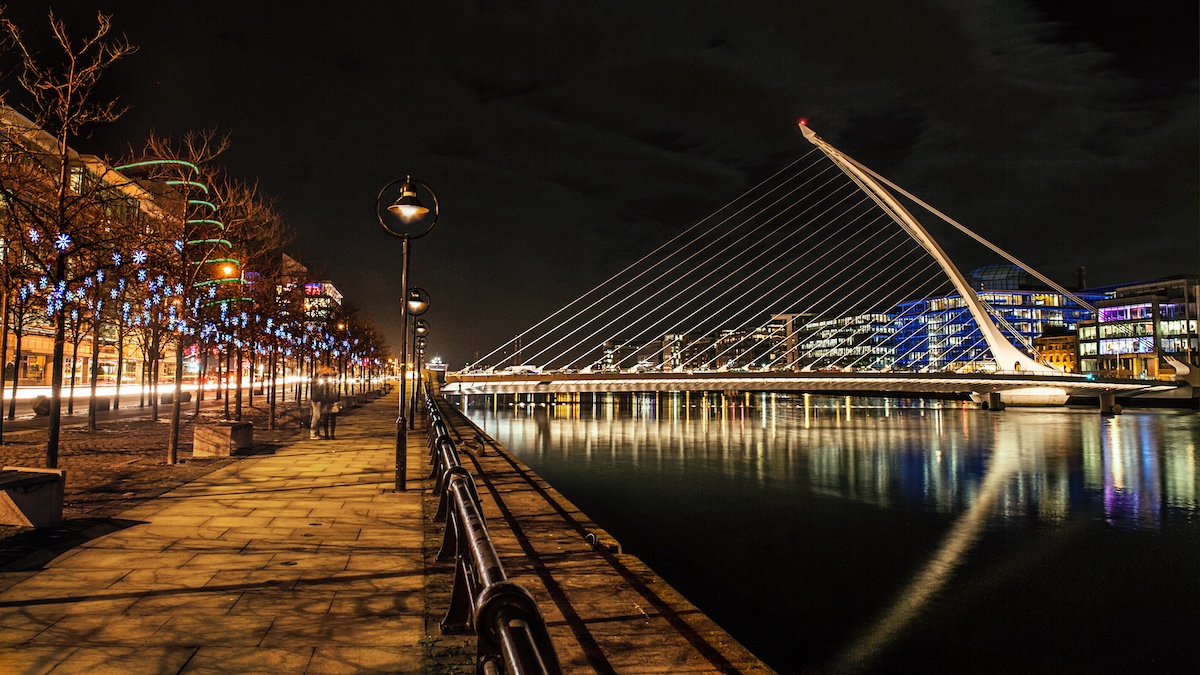 Samuel Beckett Bridge in Dublin lit up at night with festive Christmas lights along the river.