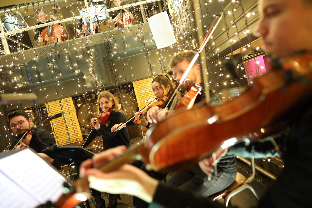 Musicians playing violins and cellos beneath festive Christmas lights at the Guinness Storehouse, Dublin.