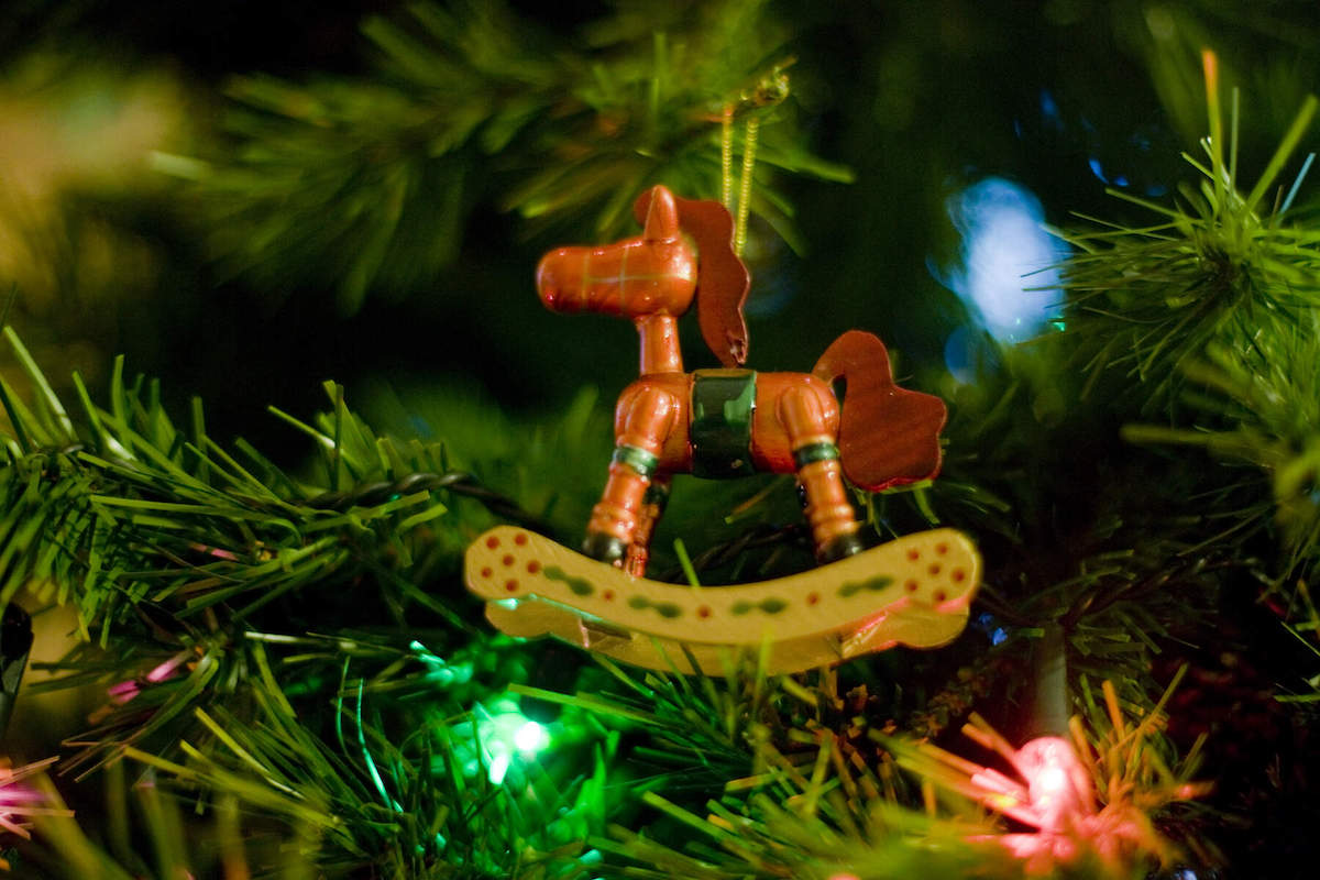 Close-up of a wooden rocking horse Christmas ornament hanging on a decorated tree.