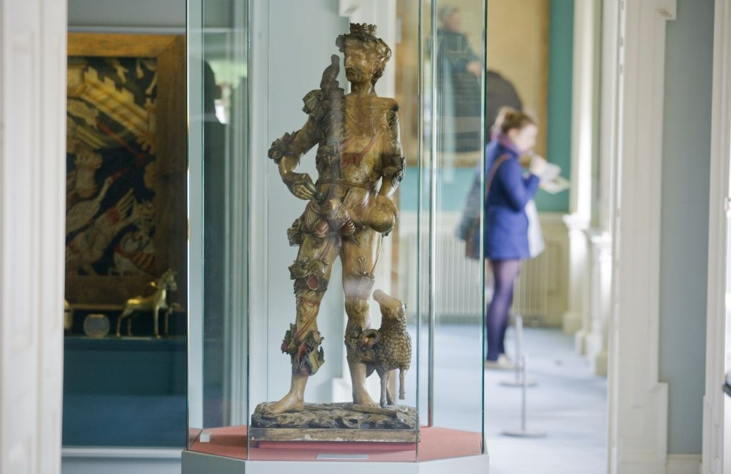 Wooden Renaissance statue of a man in glass case at the Hunt Museum, Limerick, with visitor in background.