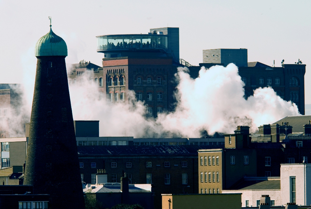 Steam rises over Dublin rooftops with the Guinness Storehouse Gravity Bar visible in the distance.