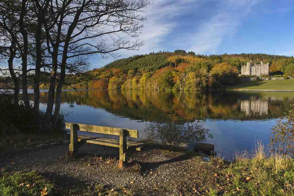 Bench overlooking Castlewellan Lake and Castle in County Down, surrounded by autumn trees and reflections.