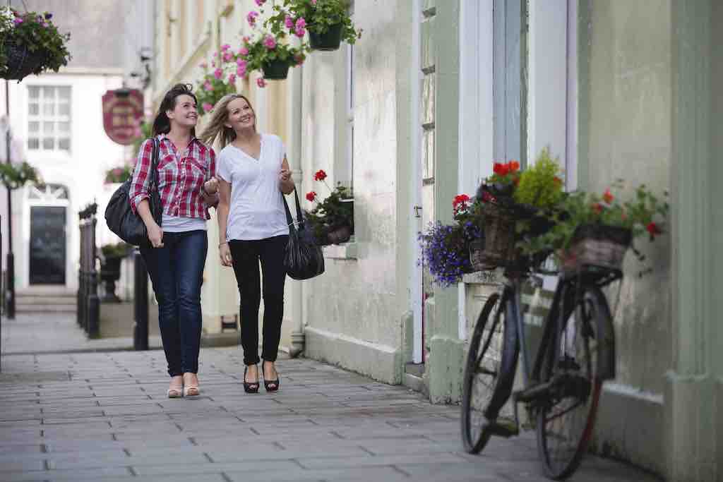 Two women walking along a flower-lined street in Moy, Northern Ireland, on a sunny day.