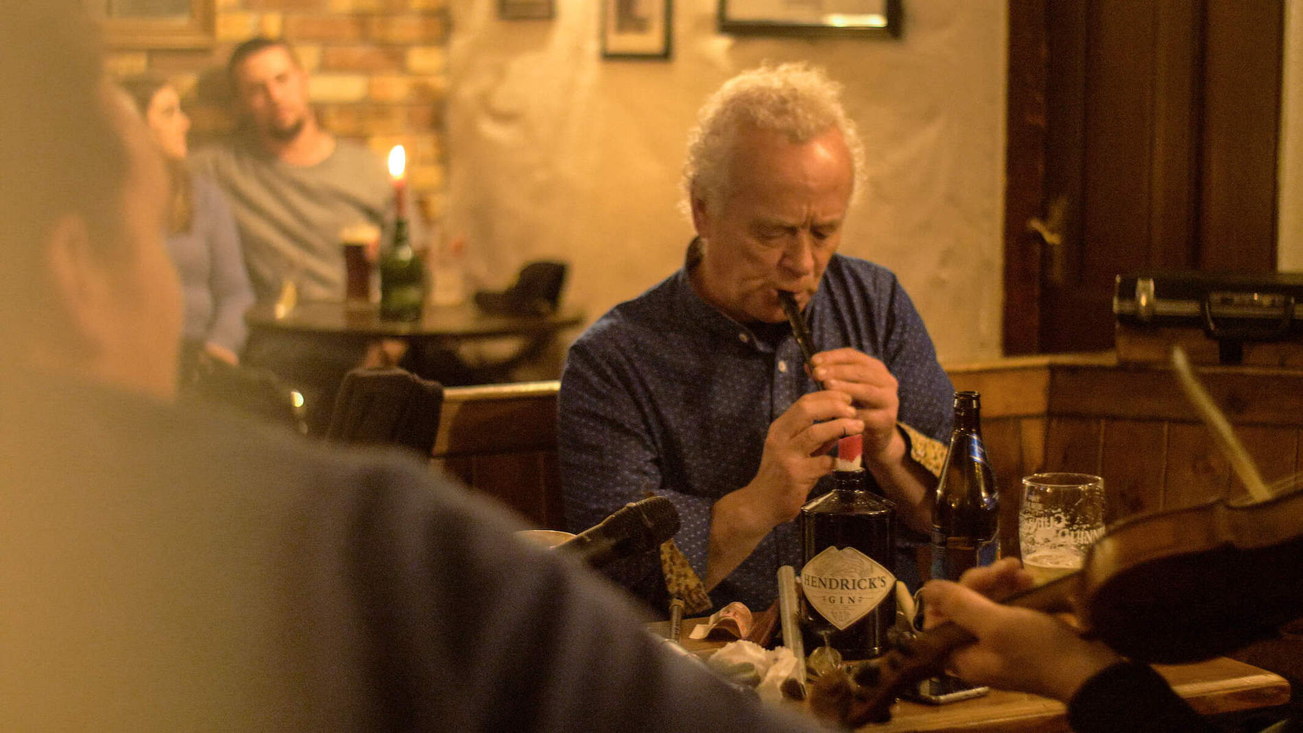 Traditional musicians at a table in a candlelit Clare pub, including a tin whistle player and others on fiddle and banjo.