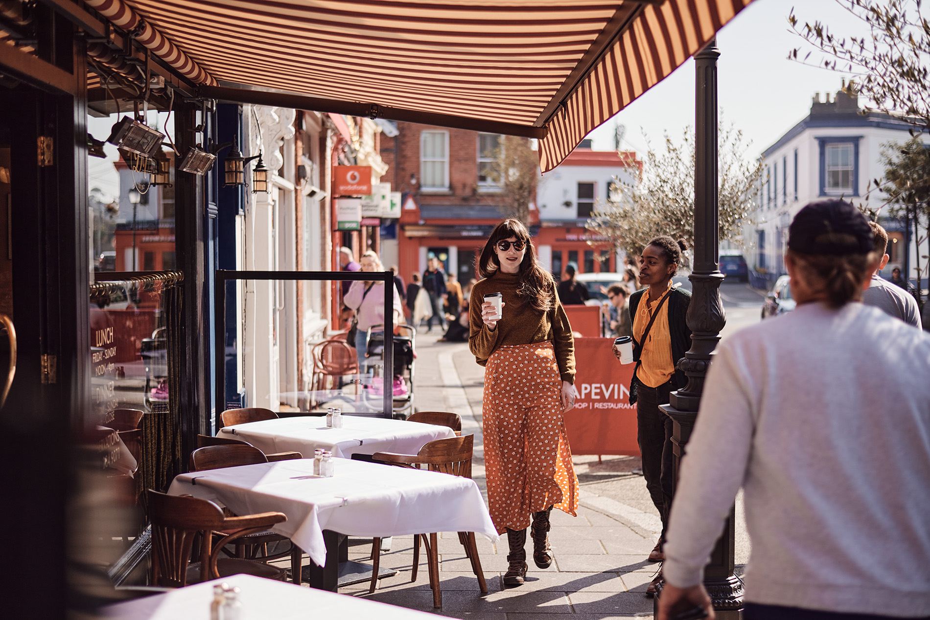 Woman in sunglasses walks with coffee on Dalkey’s main street during the Dalkey Book Festival in County Dublin.