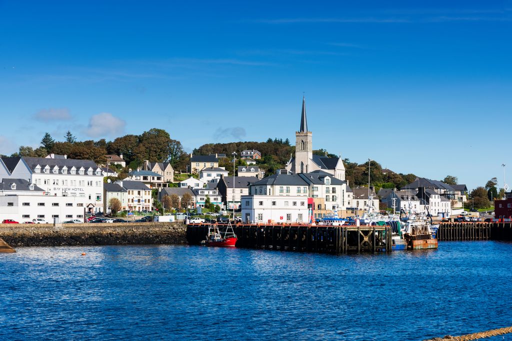 Colourful fishing boats docked beside church and houses in Killybegs harbour. 