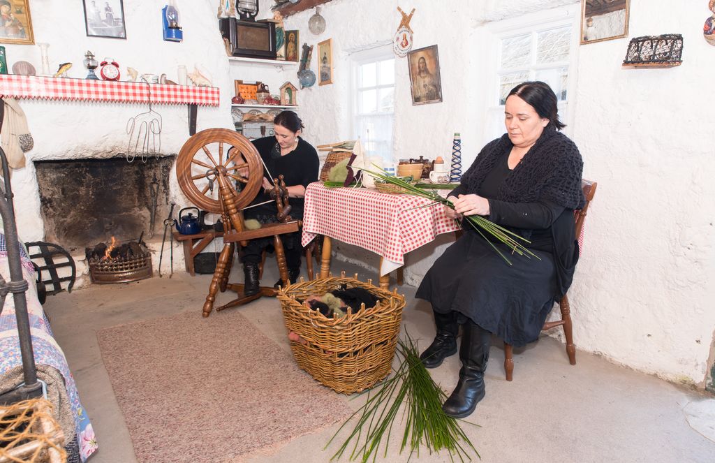 Women weaving rushes and spinning wool beside the fireplace in cottage at Colmcille Heritage Centre.