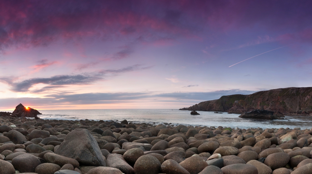 Sunset over pebble beach with waves breaking against cliffs at Bloody Foreland, County Donegal.