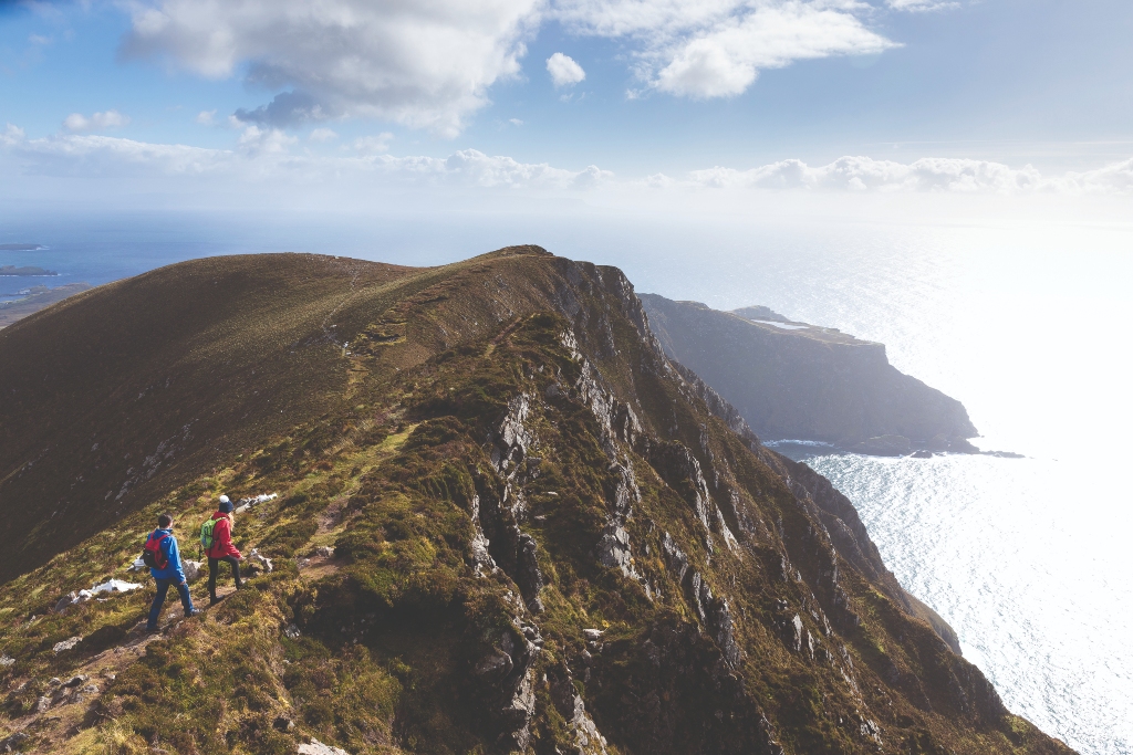 Hikers on ridge path overlooking sea cliffs at Slieve League in County Donegal.