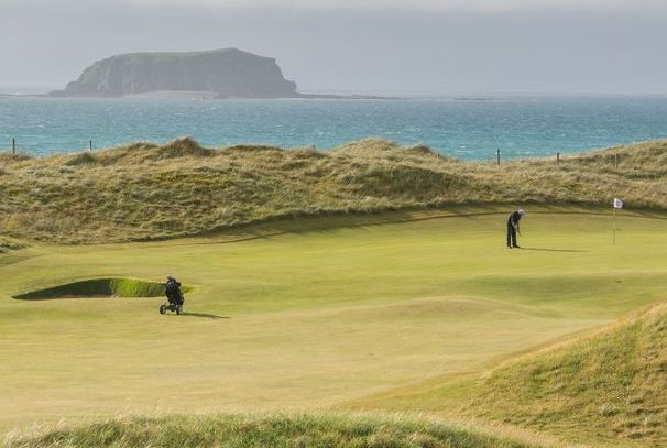 Golfer putting on links course with dunes and sea views at Portnoo Golf Club, County Donegal.
