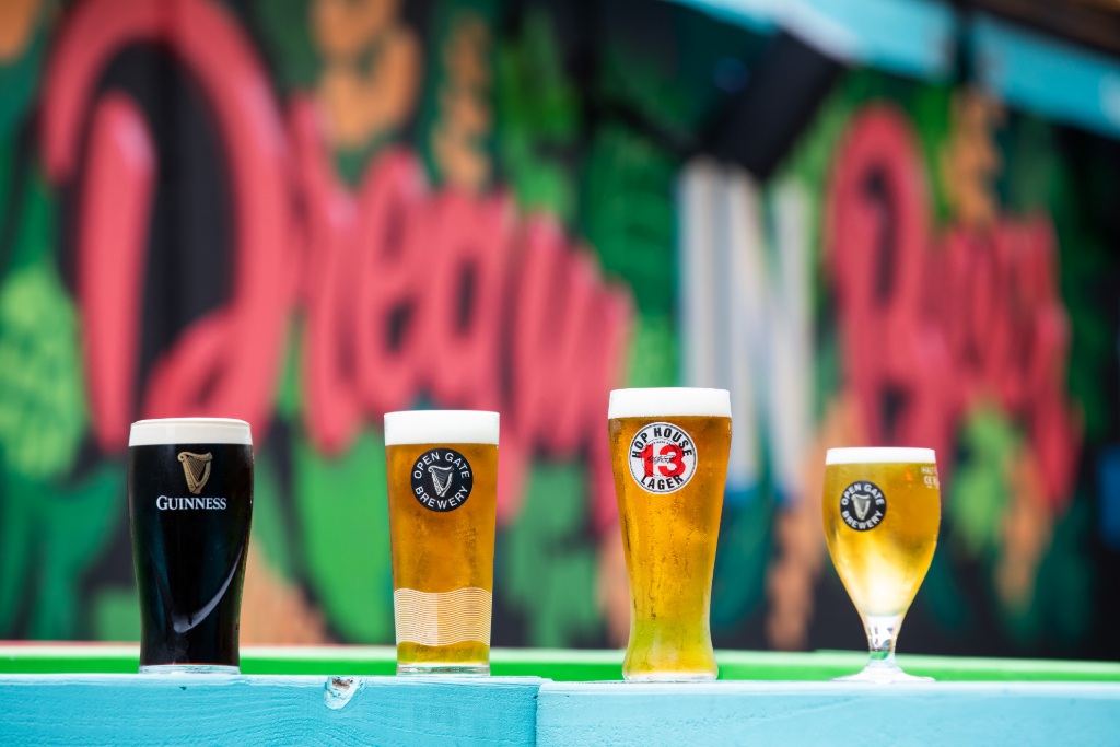 Four pints of Guinness, lager and craft beer on a bar ledge with a colourful mural backdrop.