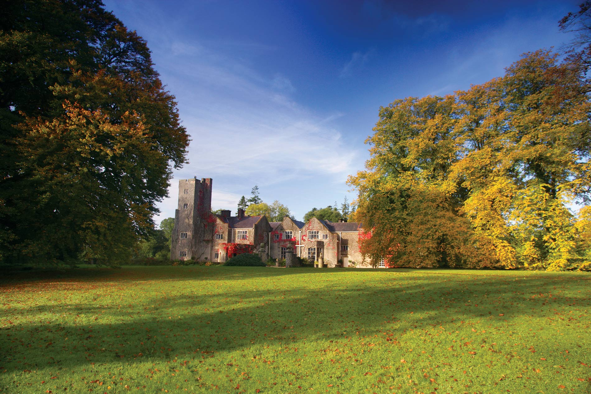 Manor house retreat framed by autumn trees at Belle Isle Estate, County Fermanagh, under a deep blue sky.