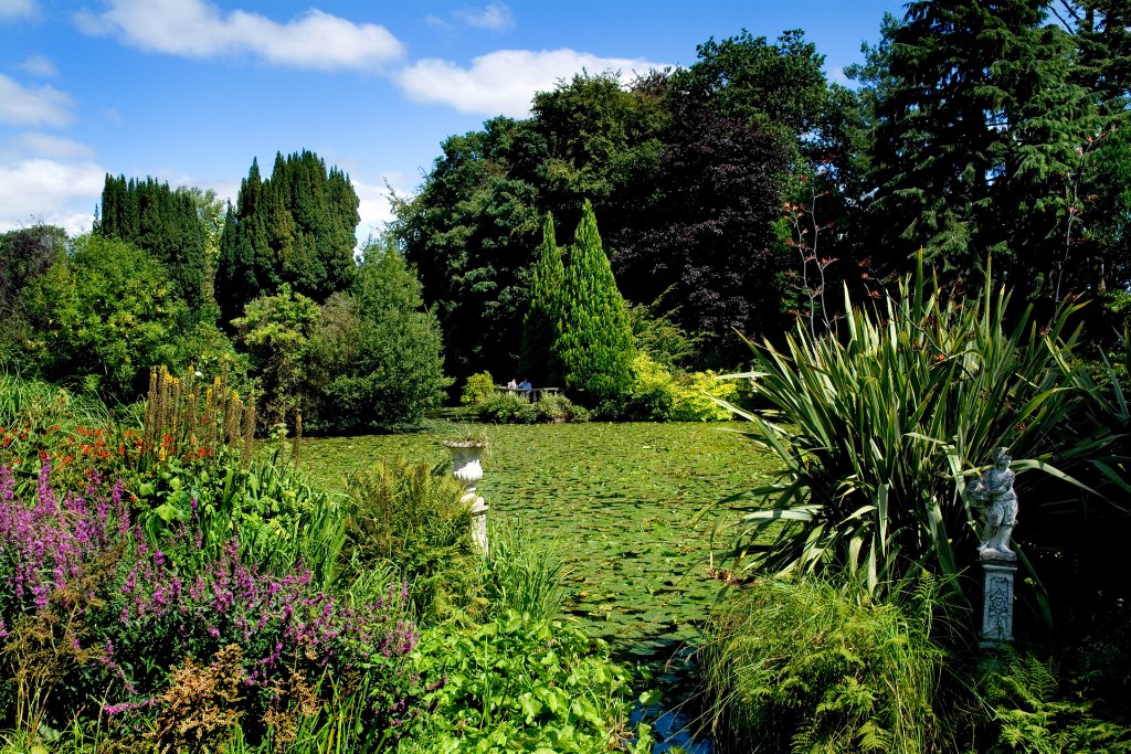 Colourful flower borders and lush greenery surrounding a lily-covered lake at Altamont Gardens.
