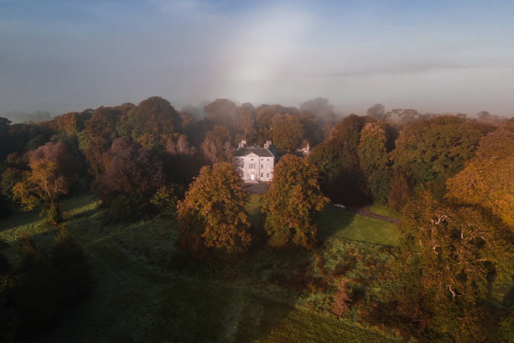 Roundwood House surrounded by tall autumn trees under misty morning light in County Laois.