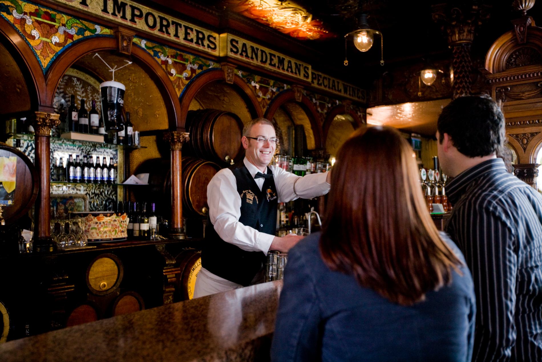 Smiling bartender serving drinks inside the ornate Crown Liquor Saloon in Belfast, Northern Ireland.