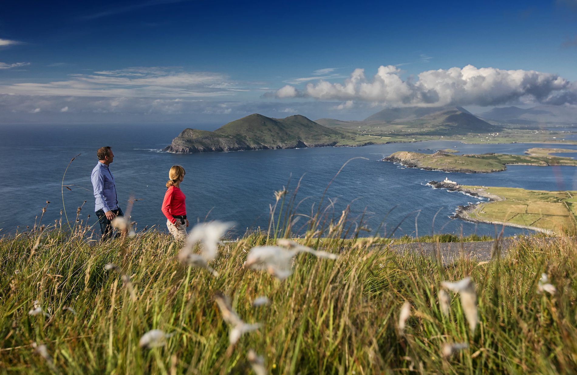 Two walkers overlook a dramatic coastline in Ireland, highlighting emergency contact information for visitors.