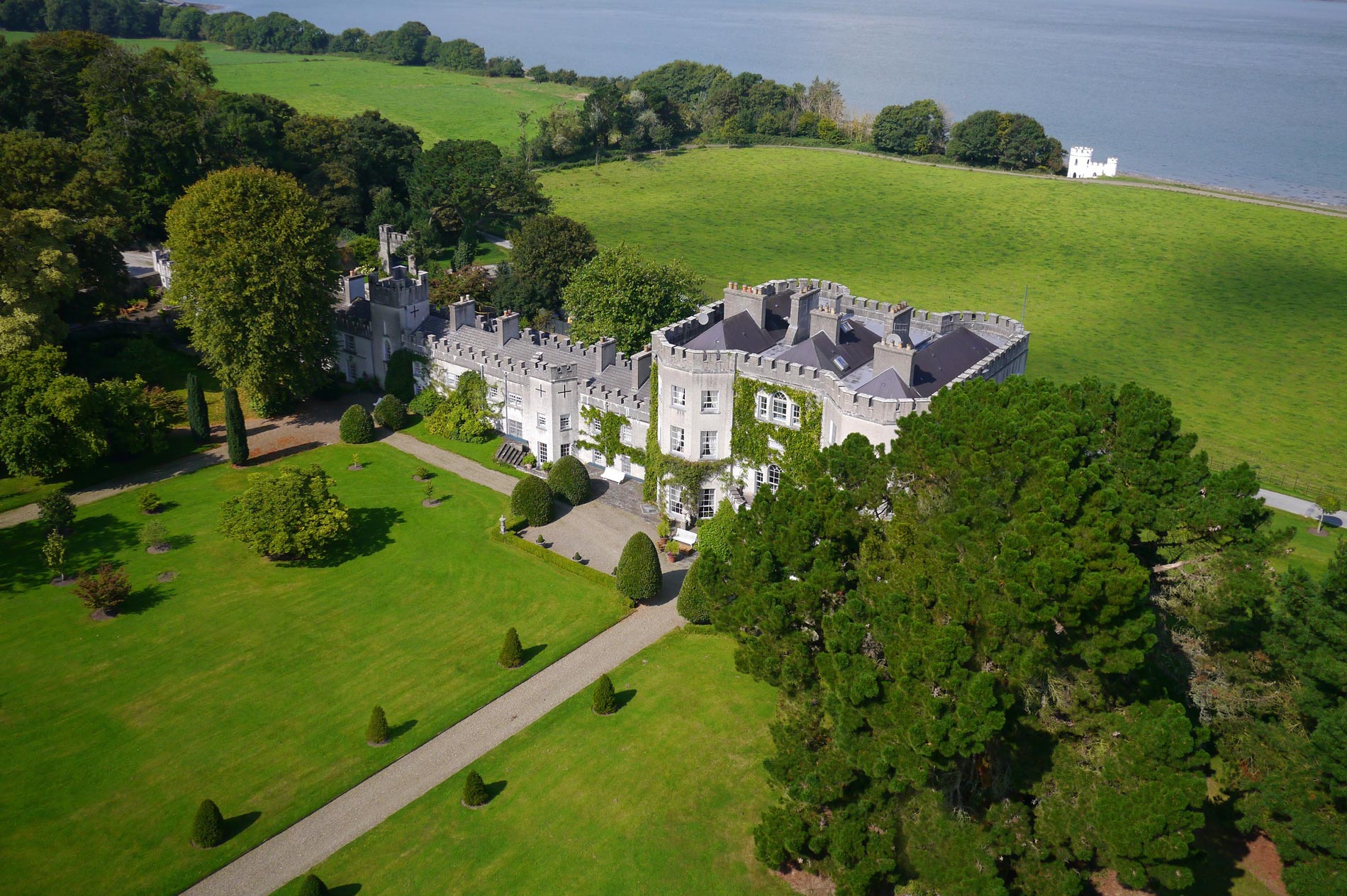 Aerial view of an Irish castle surrounded by lawns and trees under a clear blue sky.