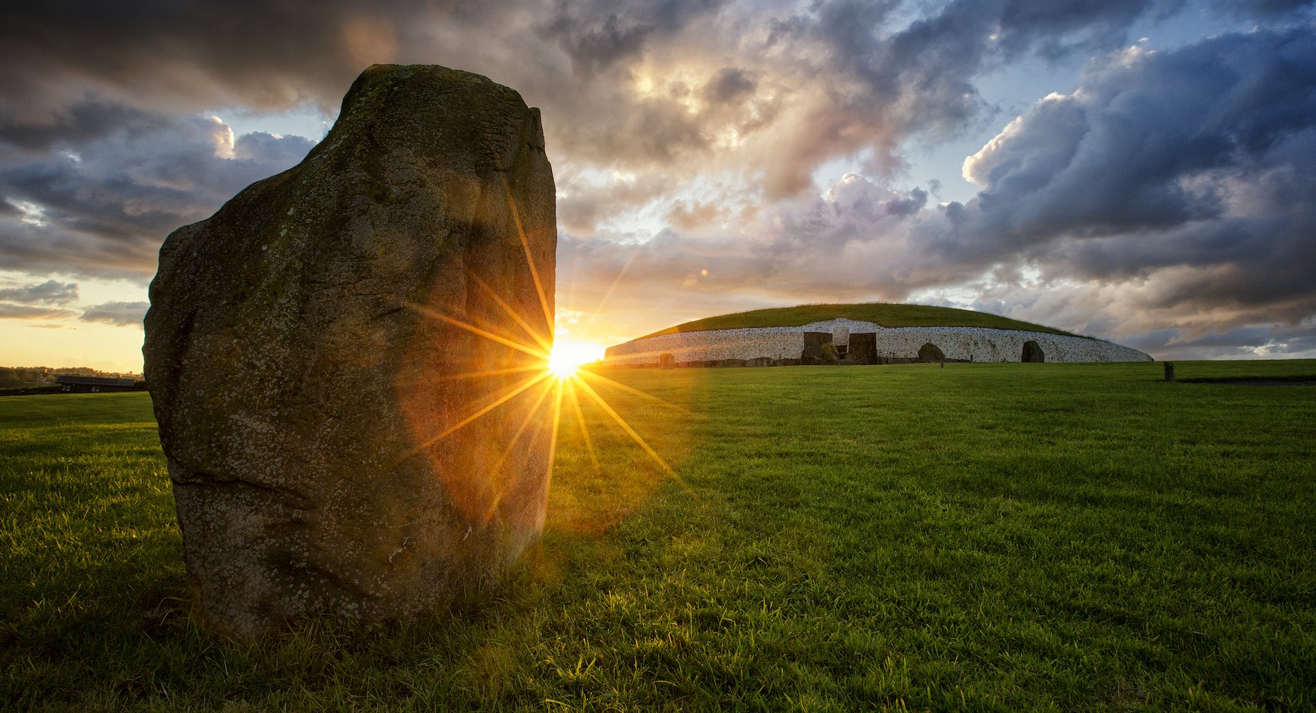 Sunrise at Newgrange, with light shining past a standing stone and illuminating the ancient mound.