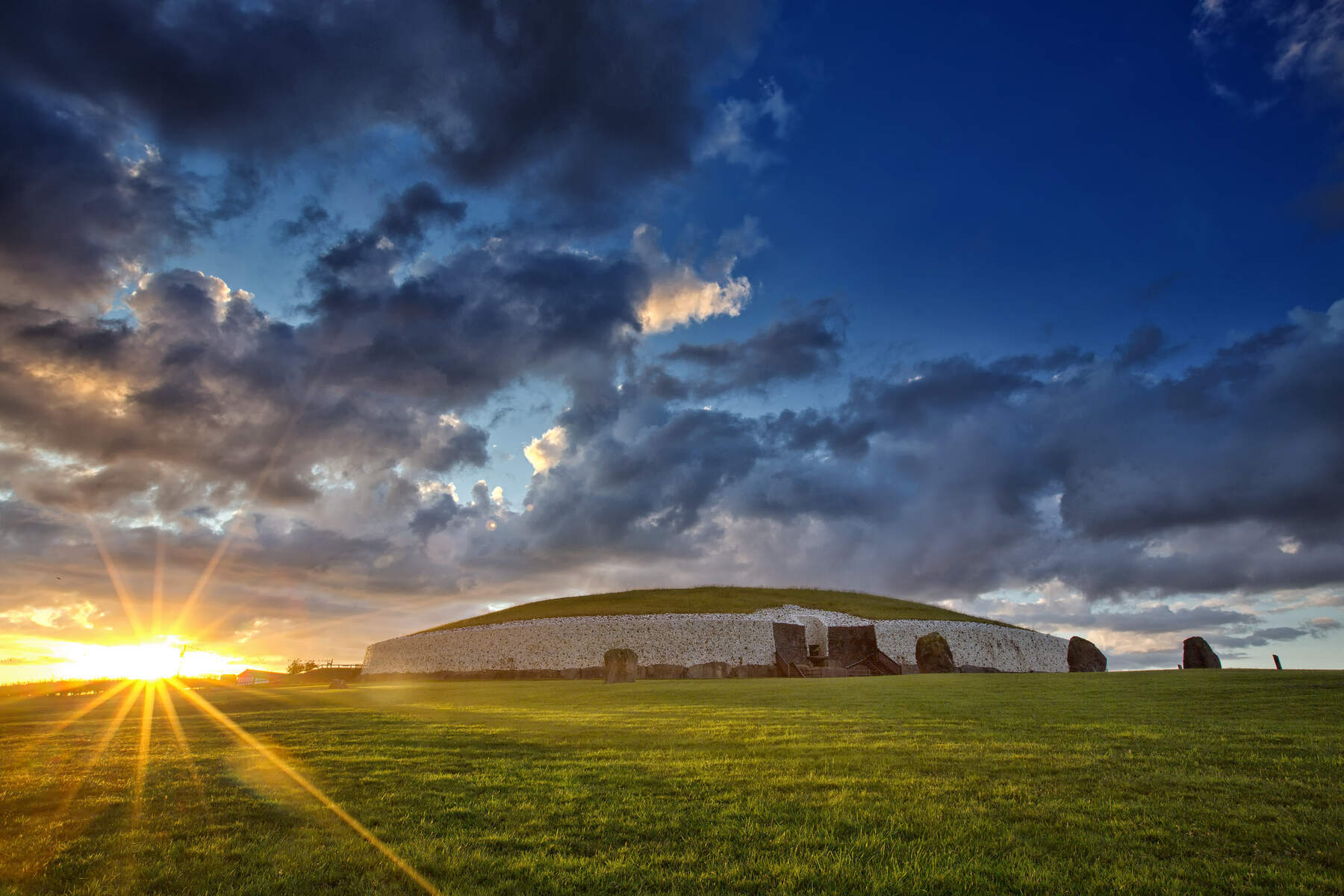 Winter sunrise casting golden light over Newgrange’s grass-covered mound and stone entrance.