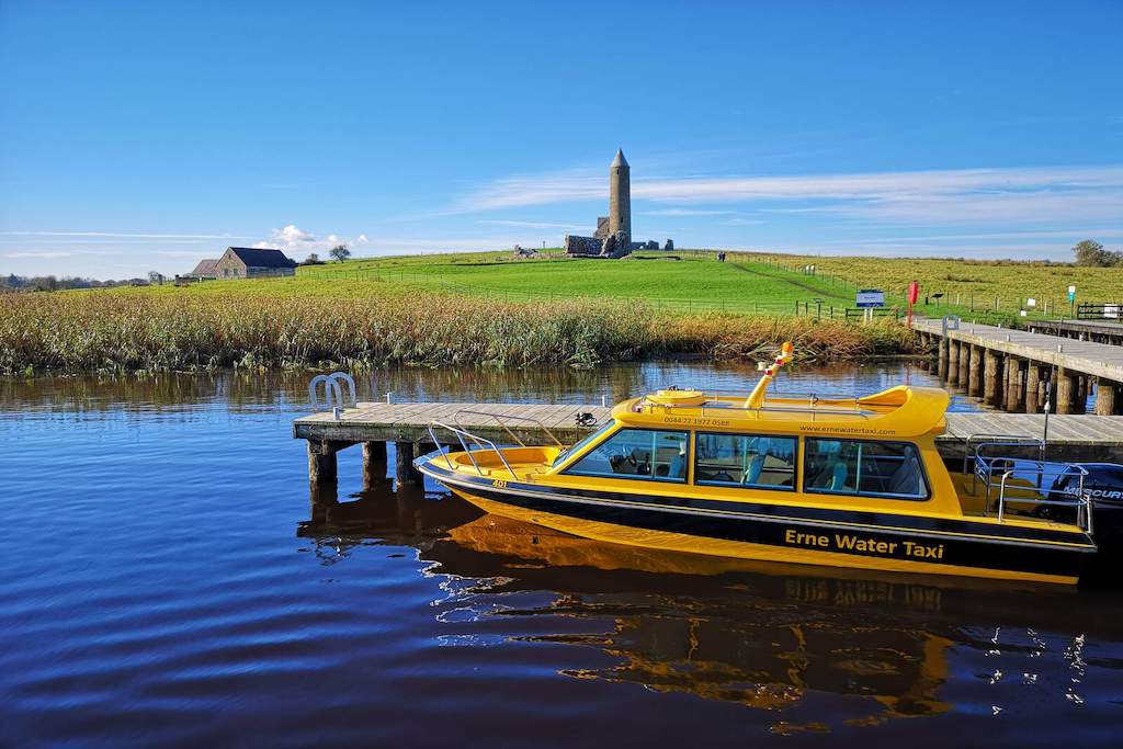 The Erne Water Taxi moored near Devenish Island, with its historic round tower and church ruins visible on the hill.