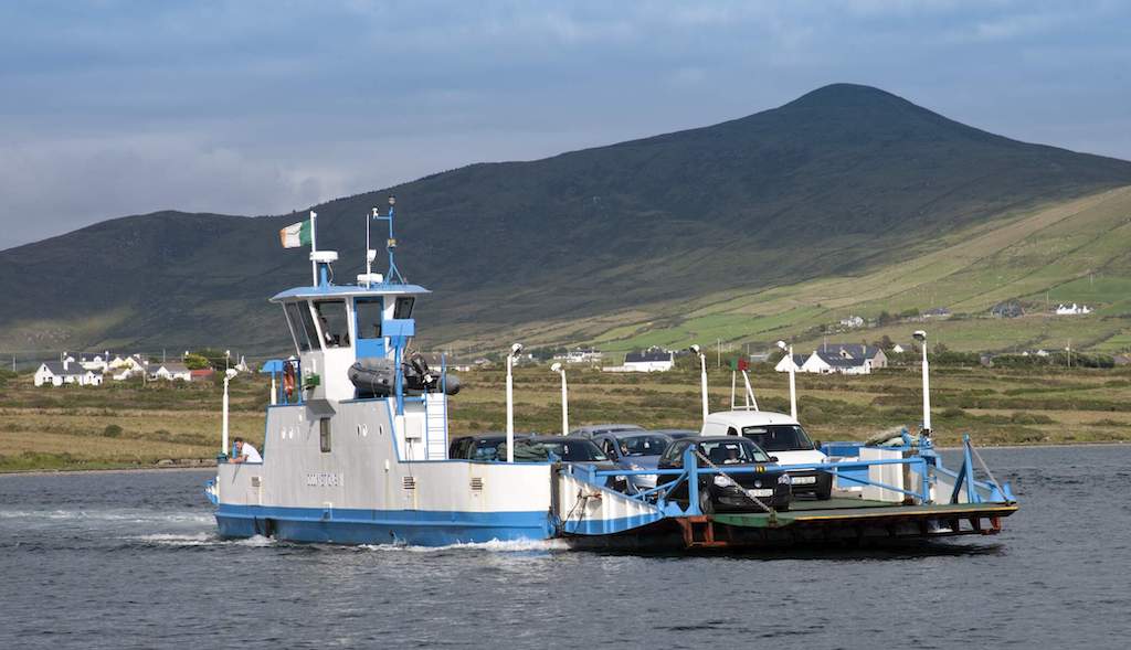Car ferry transporting vehicles between Valentia Island and County Kerry, with green hills in view.