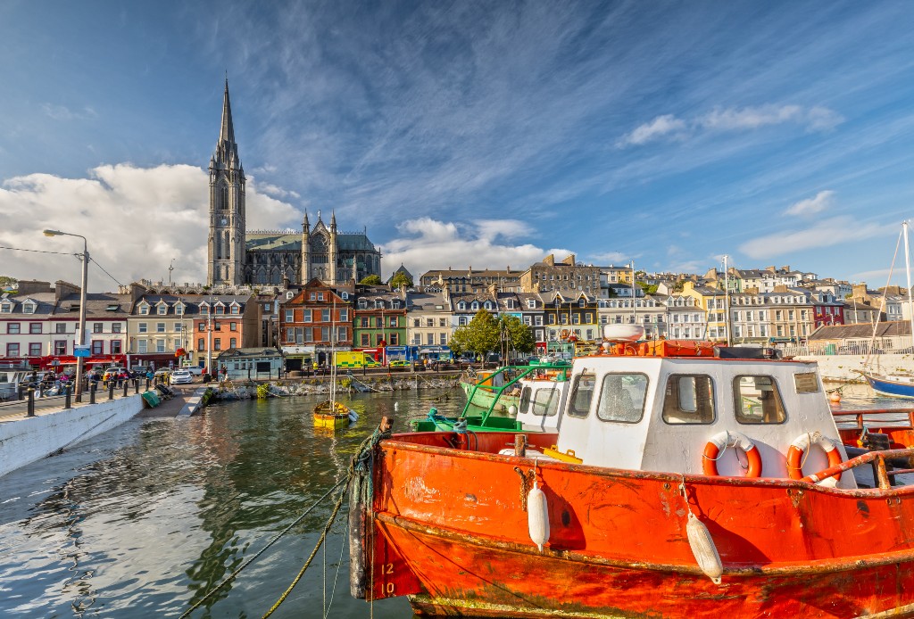 Colourful boats in Cobh Harbour, County Cork, with St Colman’s Cathedral towering over the vibrant waterfront buildings.