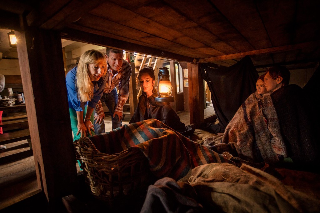 Visitors explore the dimly lit cabin of the Dunbrody Famine Ship in County Wexford beside costumed interpreters.