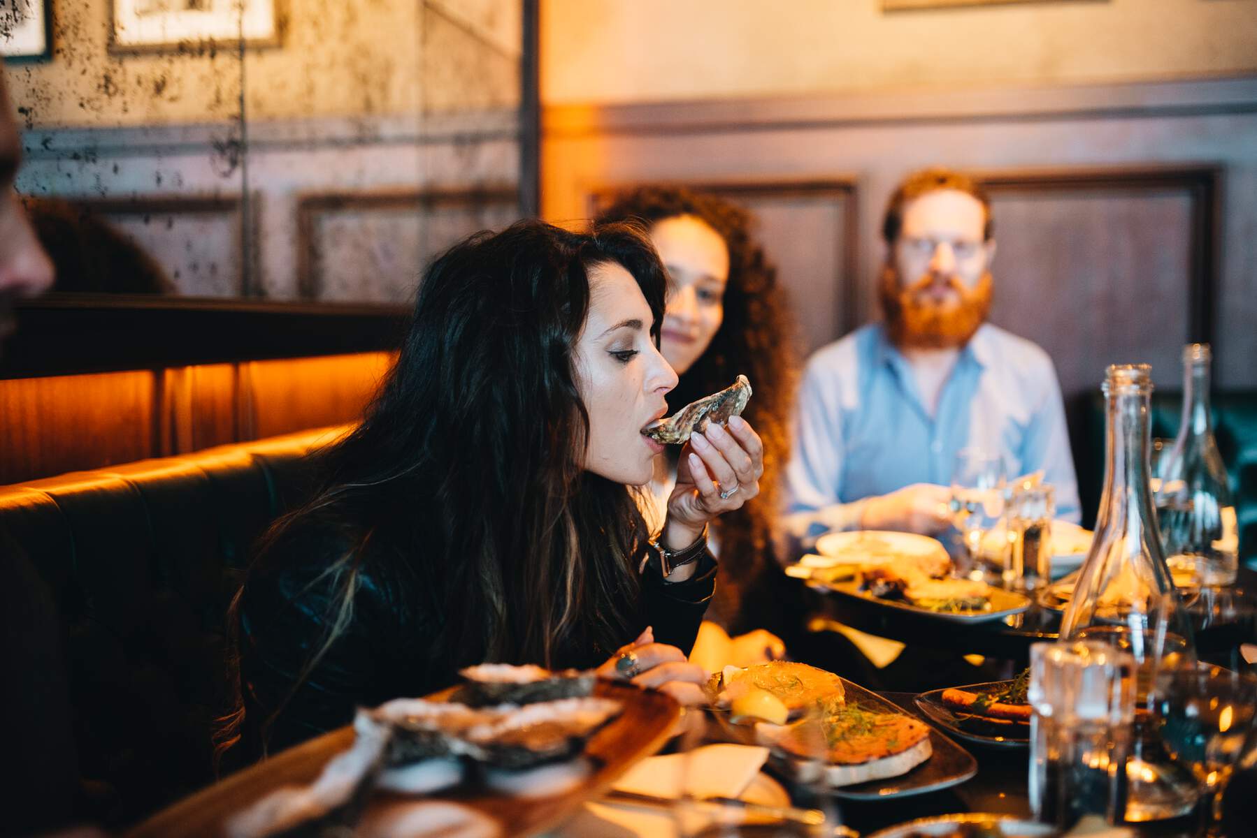 Woman eating an oyster at a restaurant with friends in Ireland.