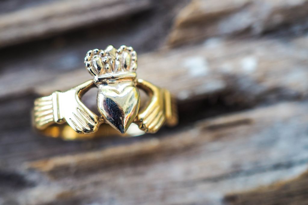 Close-up of a gold Claddagh ring featuring hands, heart and crown, placed on rustic wooden surface.