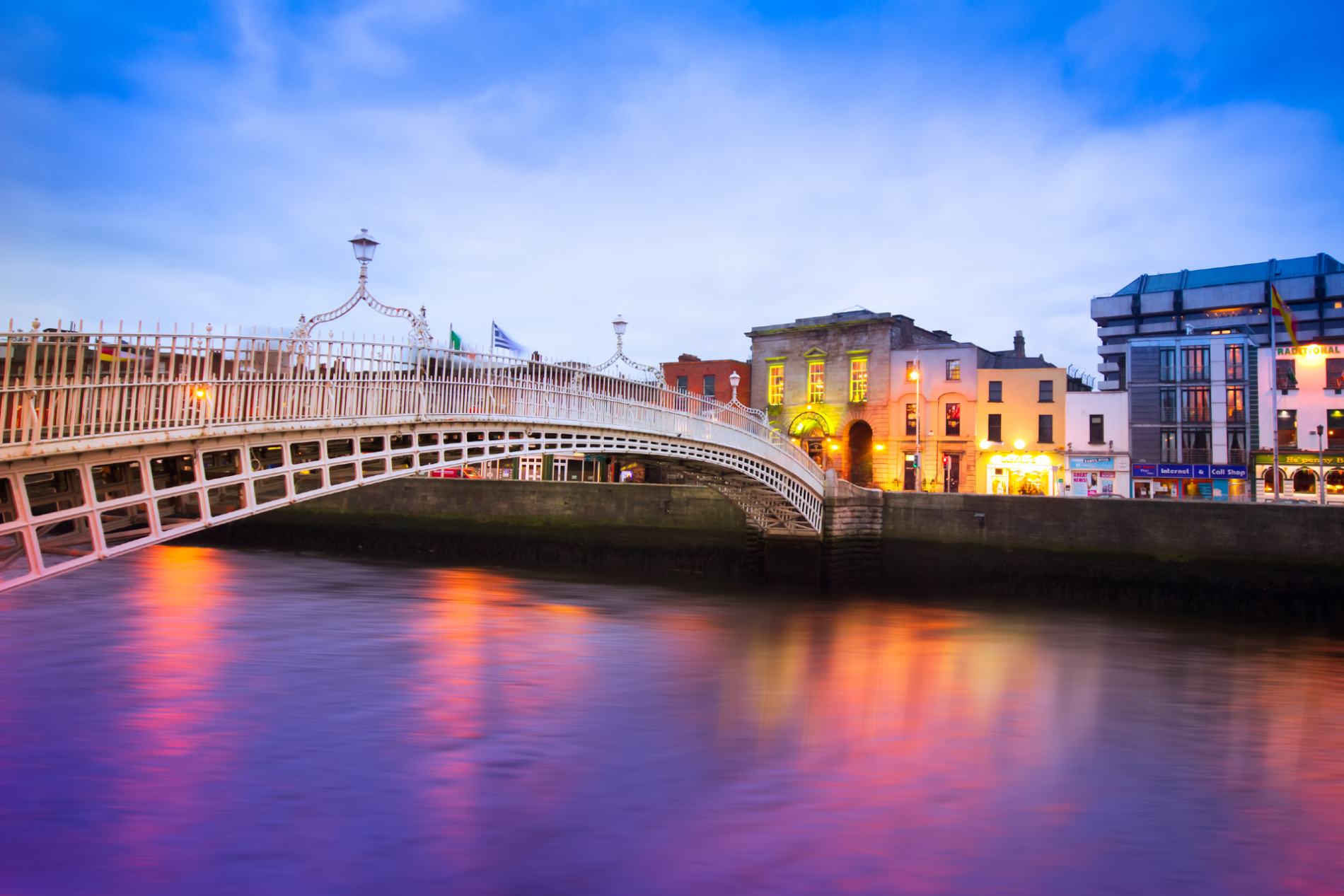 Twilight view of Dublin’s Ha’penny Bridge lit in gold, city lights glowing behind.