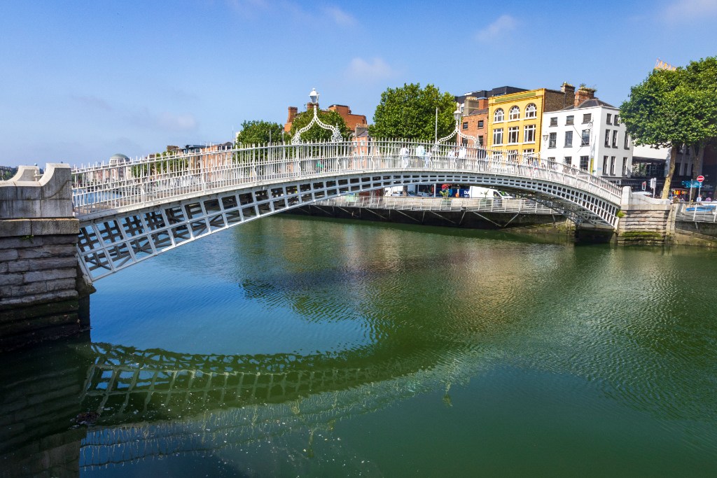 Morning view of Ha’penny Bridge over River Liffey, with Georgian buildings and reflections in calm water.