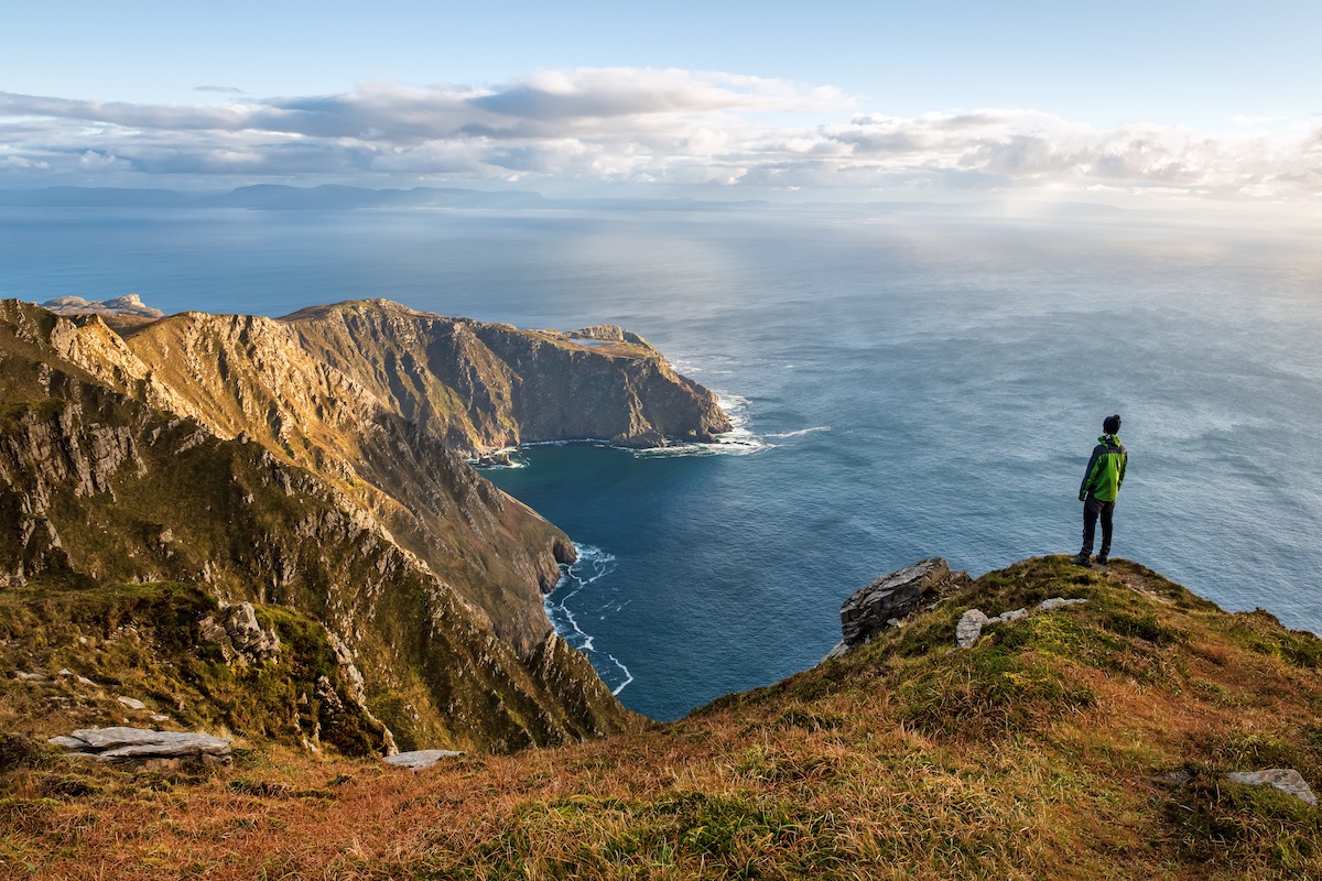 Hiker standing at Slieve League cliffs in County Donegal, gazing over the Atlantic Ocean.