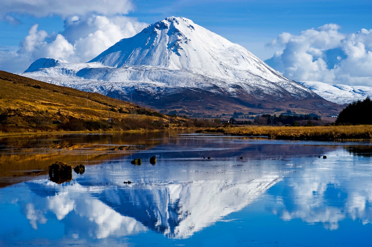 Snow-covered Mount Errigal reflected in still water at its base in County Donegal.