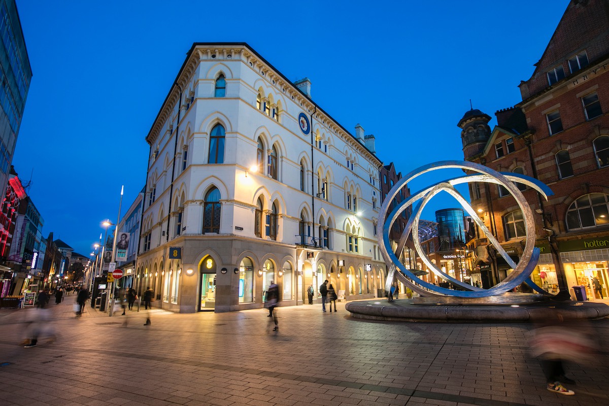 Belfast city centre at dusk with shops, historic buildings and the Spirit of Belfast sculpture.