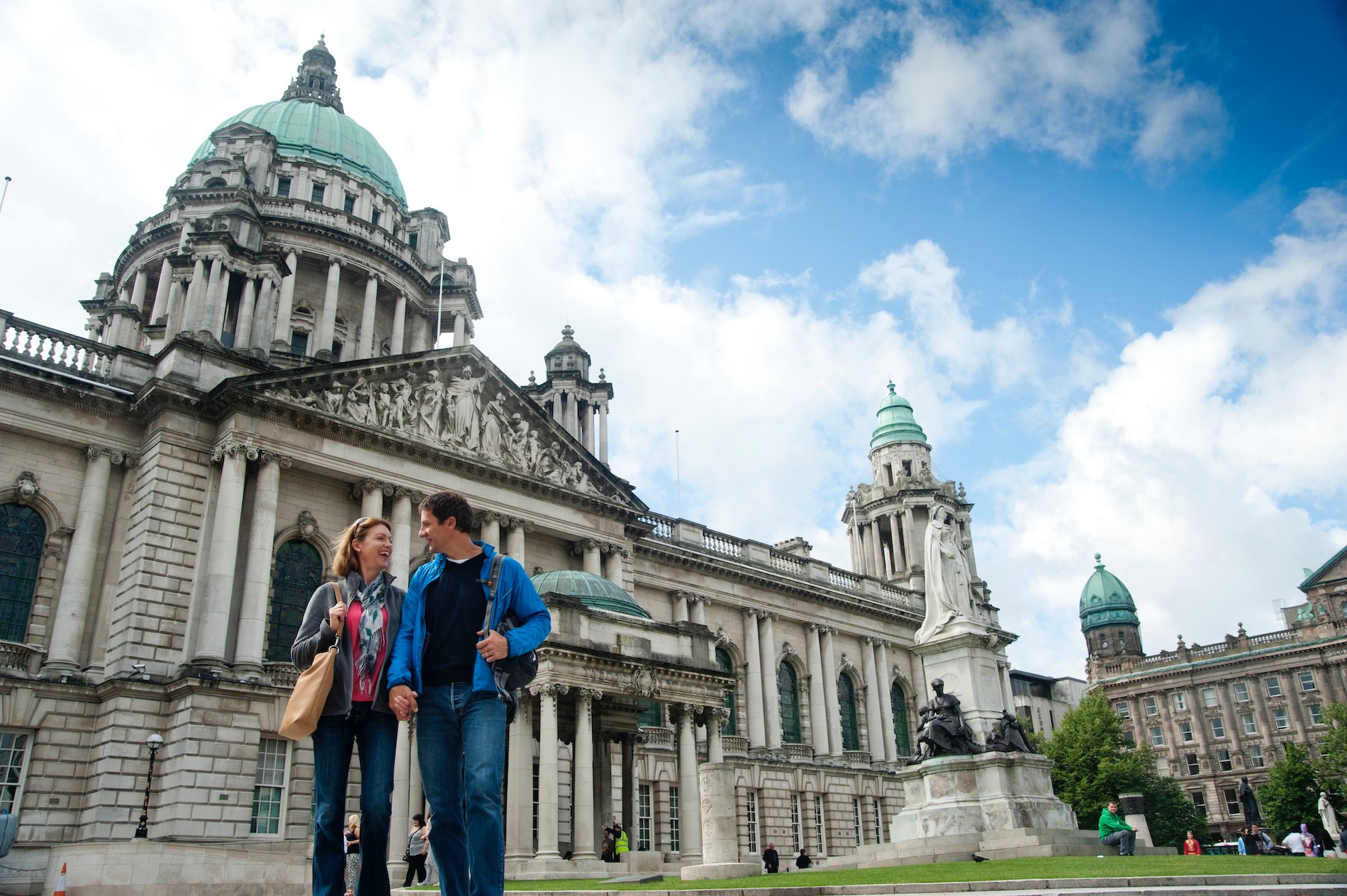 Couple outside Belfast City Hall, a landmark with green dome and ornate stone architecture.
