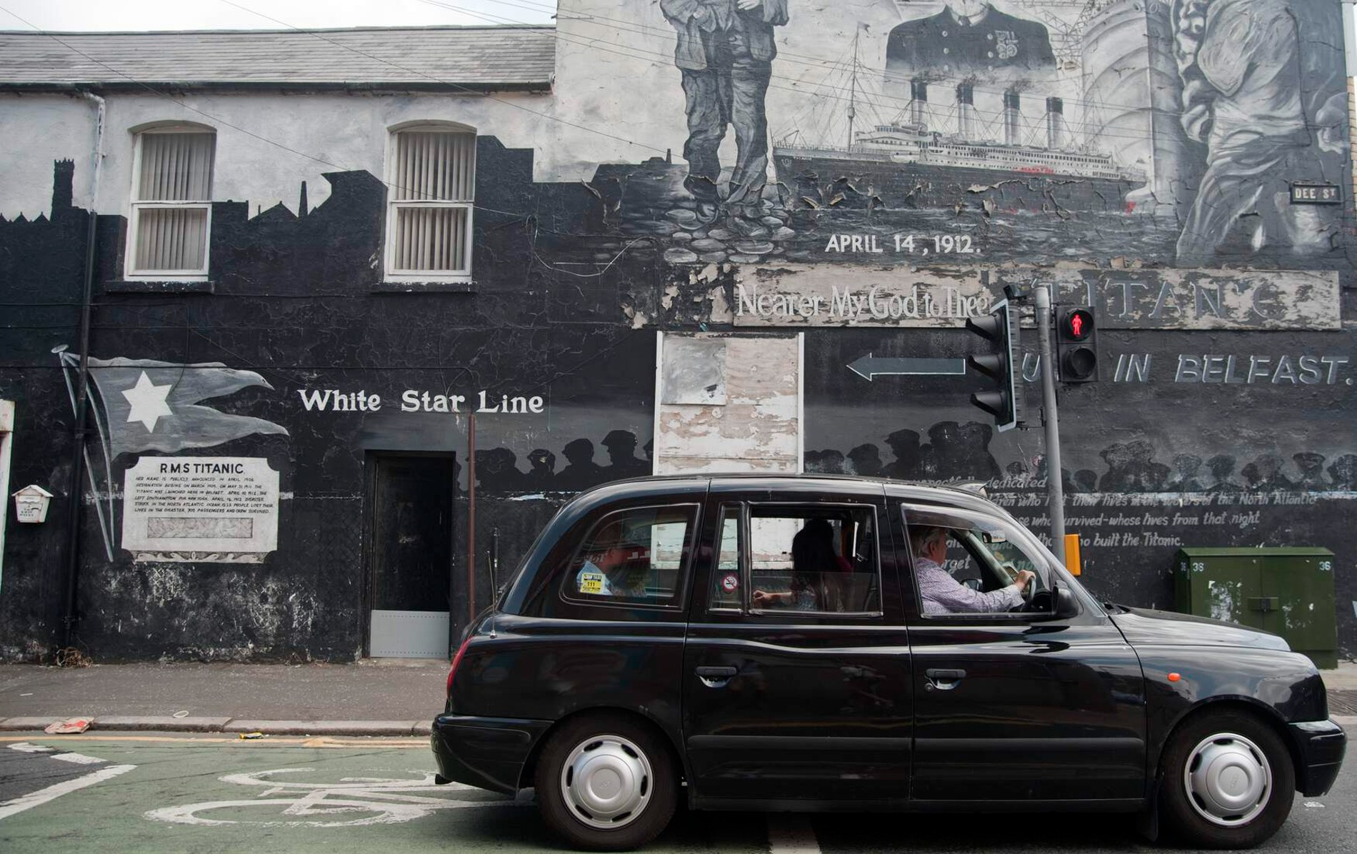 Black taxi drives past a Titanic mural on a gable wall in East Belfast commemorating the 1912 tragedy.