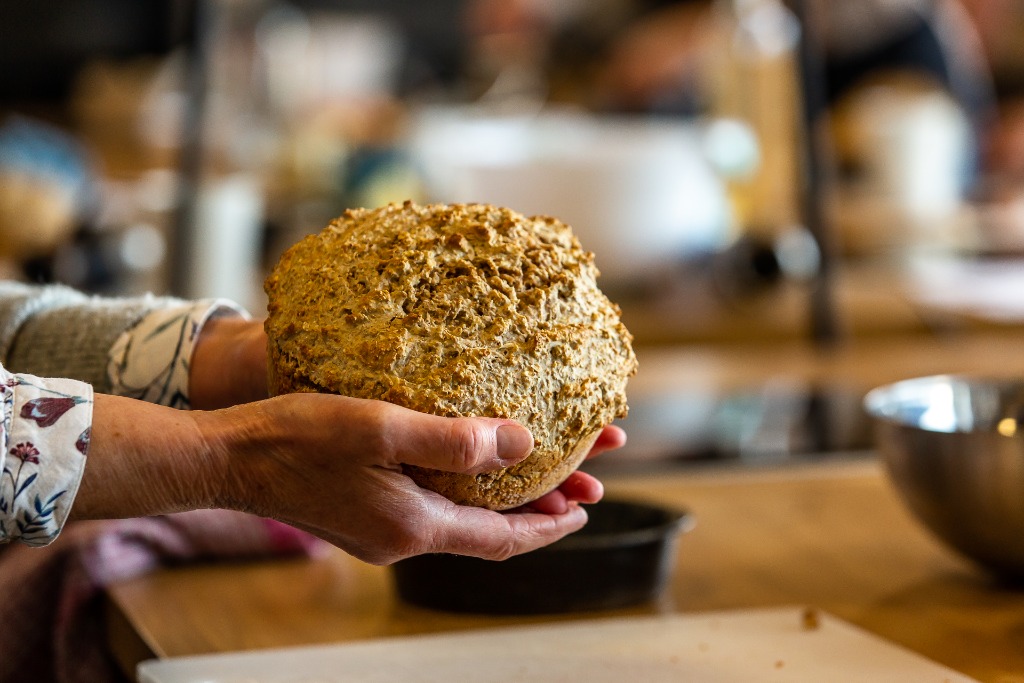 Close-up of fresh Irish brown soda bread held by a baker in a cookery class kitchen.