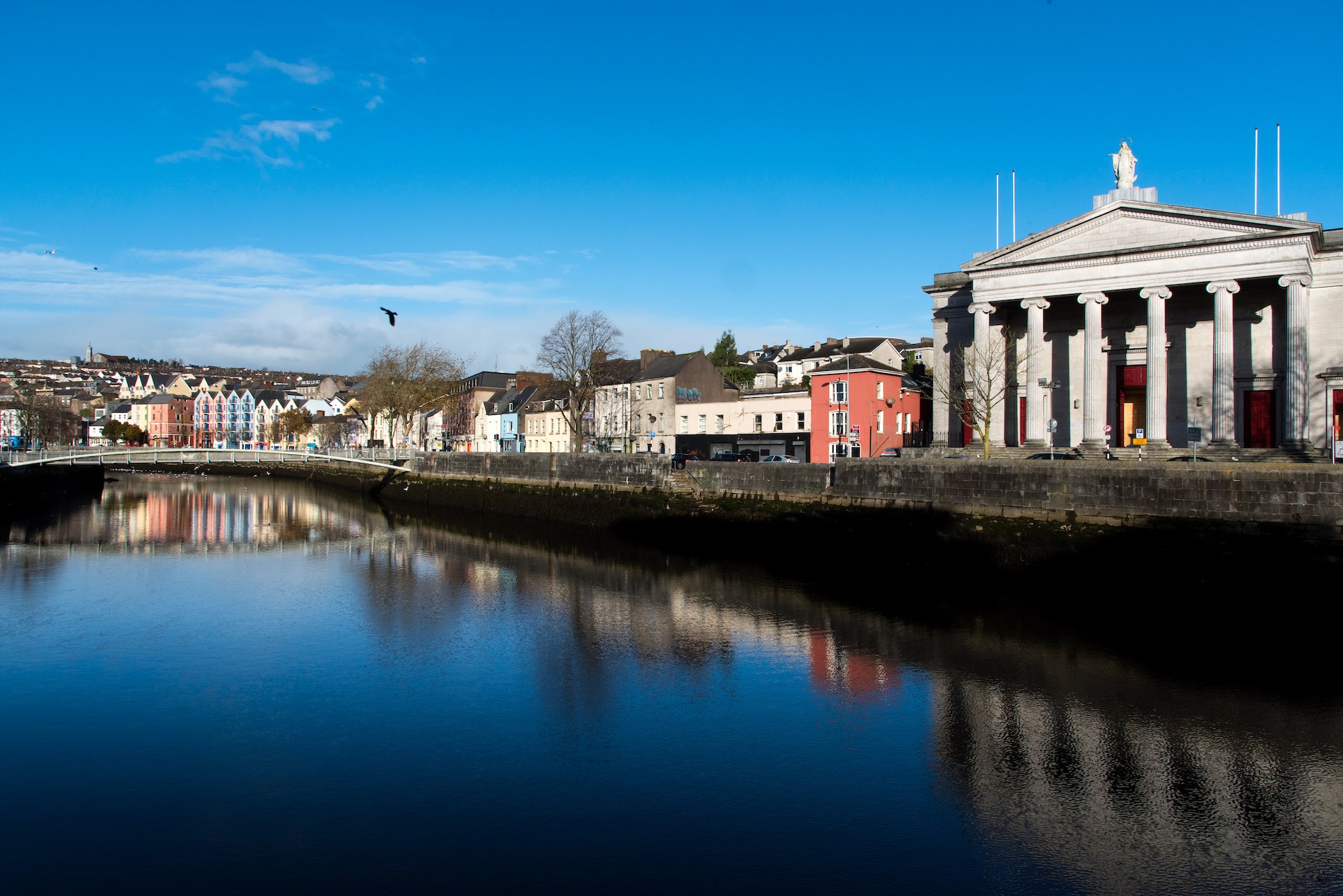 Colourful riverside buildings and a neoclassical courthouse reflected in the River Lee.
