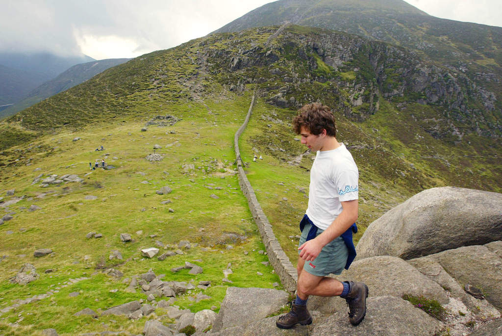 Walker steps along the Mourne Wall as it winds through the rugged landscape of the Mourne Mountains, County Down.