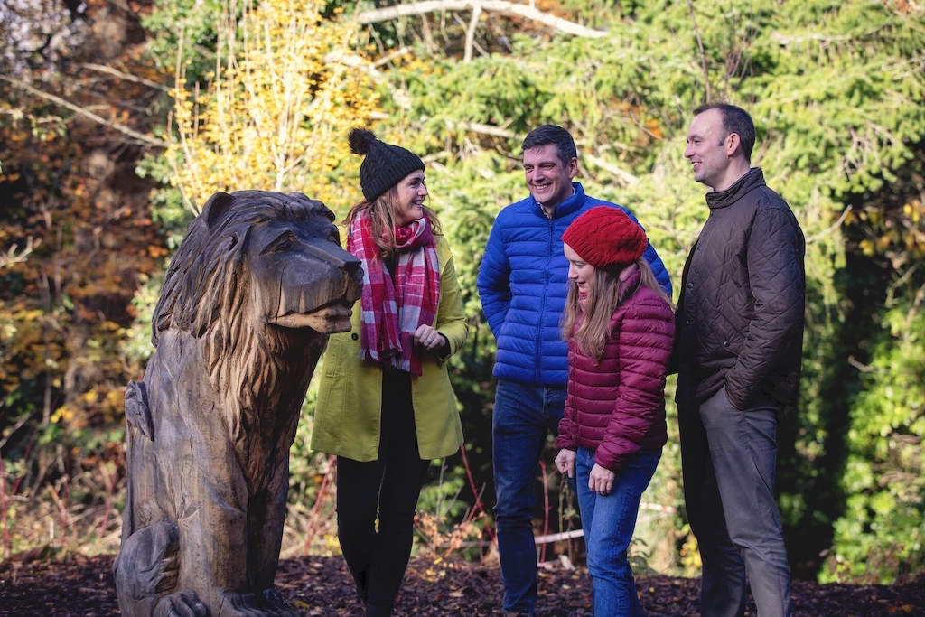 Family gathers around carved lion sculpture on the Narnia Trail in Kilbroney Forest Park, County Down.