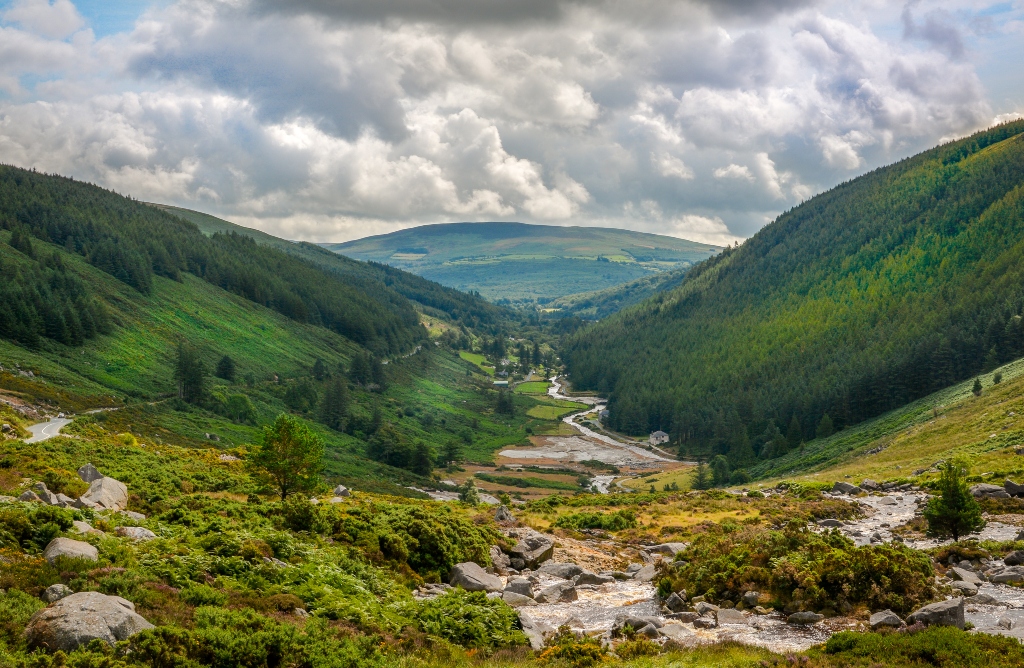 A lush green valley with a winding river running through Glendalough in County Wicklow.