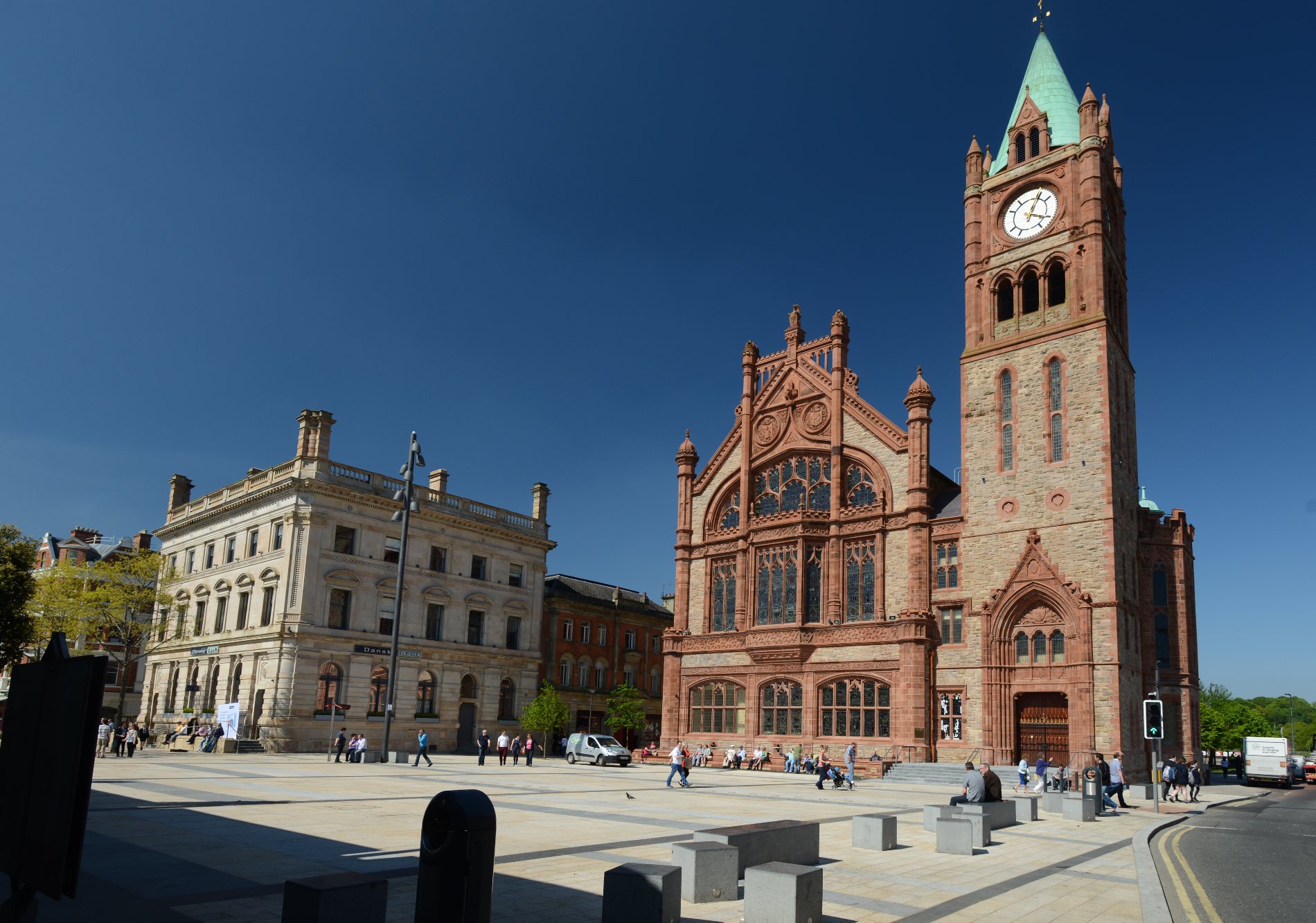 Derry~Londonderry’s Guildhall with red sandstone façade and clock tower rises against a blue sky, seen from Guildhall Square.
