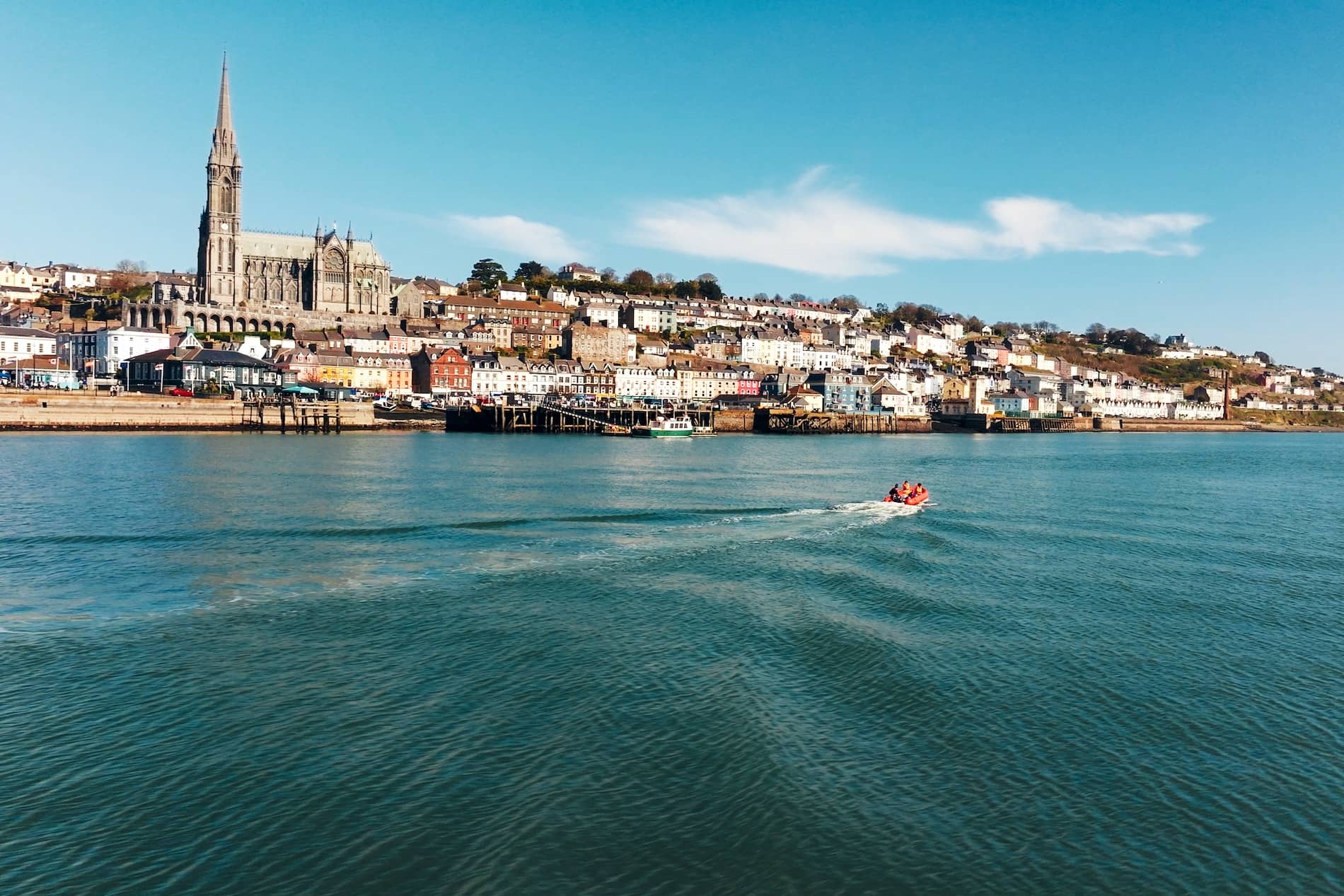 Cobh harbour and St Colman’s Cathedral, County Cork, with colourful waterfront and boat on calm water.